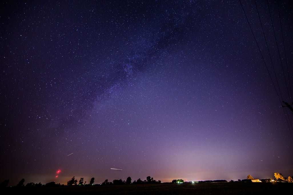 a couple of streaks of light are seen near the horizon in a starry sky that appears purple