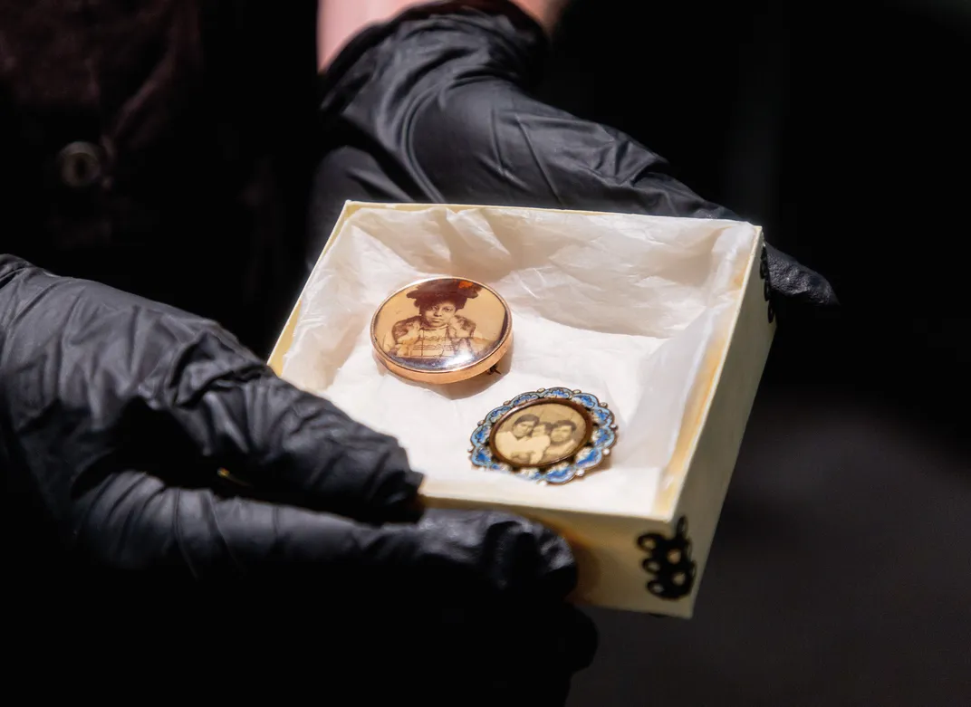 black gloved hands hold a box with two celluloid portraits