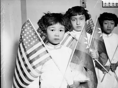 Group portrait of three Chinese children, each holding an American flag and a Chinese flag, in a room in Chicago, 1929
