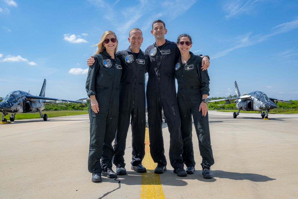 Four people in blue suits stand on a runway