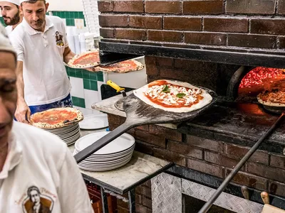 The main oven at Pizzeria Da Michele is near customers’ tables. The waiter in the background holds marinaras.