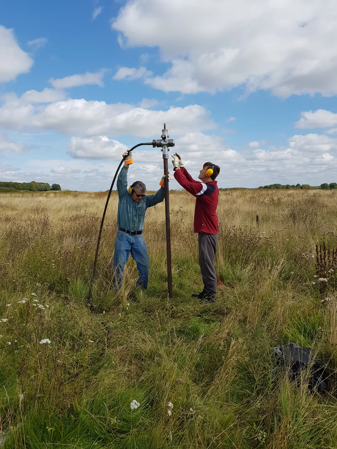 Two men holding up a piece of equipment in a grassy field