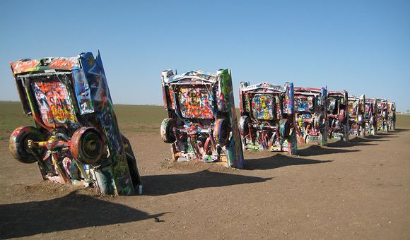 A group of 8 to 10 Cadillac cars half buried appear in a row with graffiti paint on them