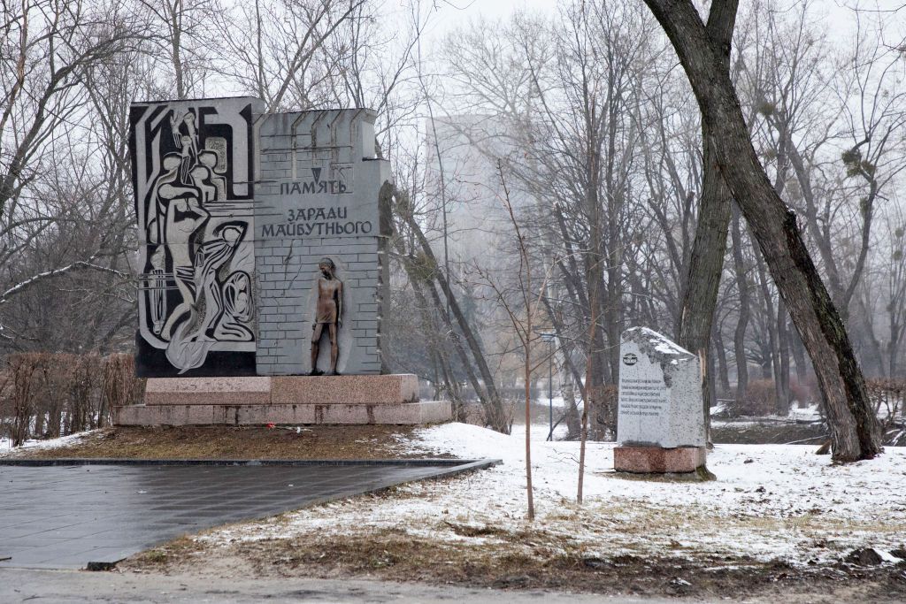 snowy view of a monument with a bronze statue of a man standing in front of a wall with Ukrainian writing
