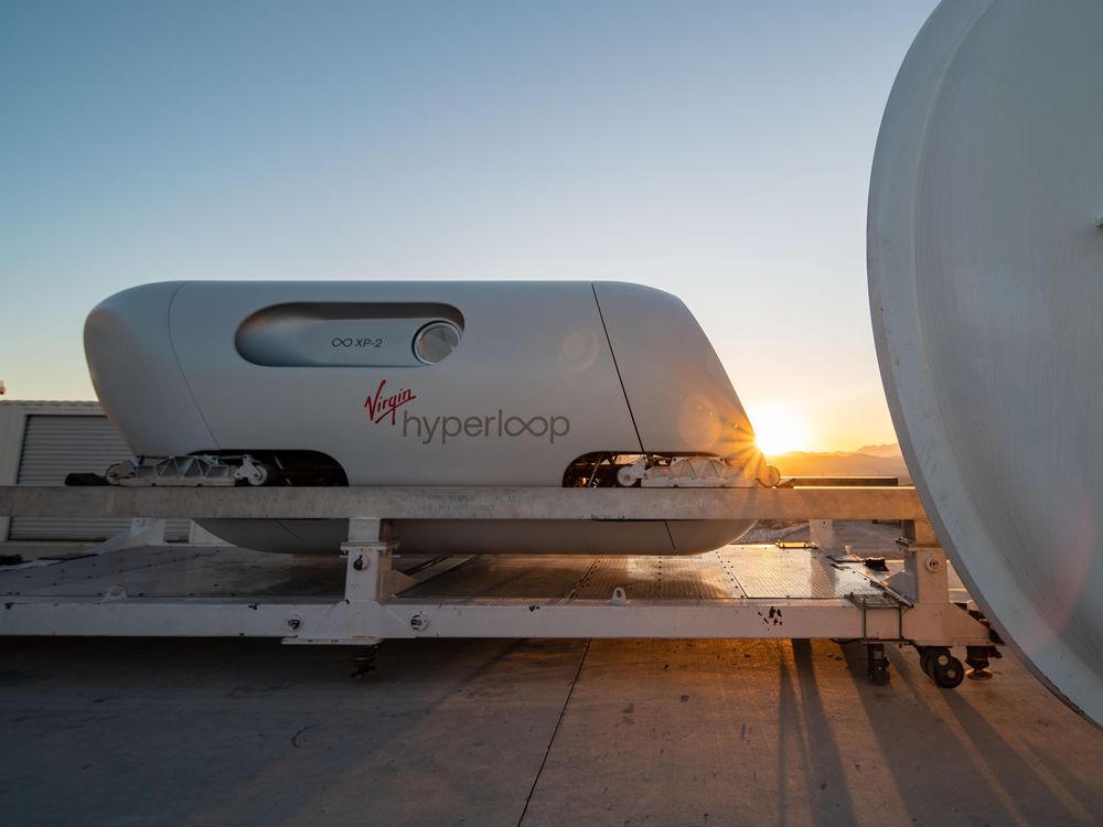 The image shows a white transportaion vehicle on a track with the sun setting behind it. 