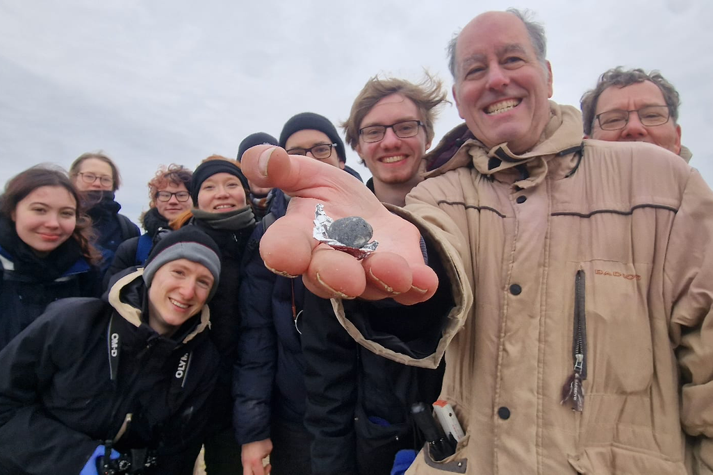 about ten people smiling with one holding a very small rock
