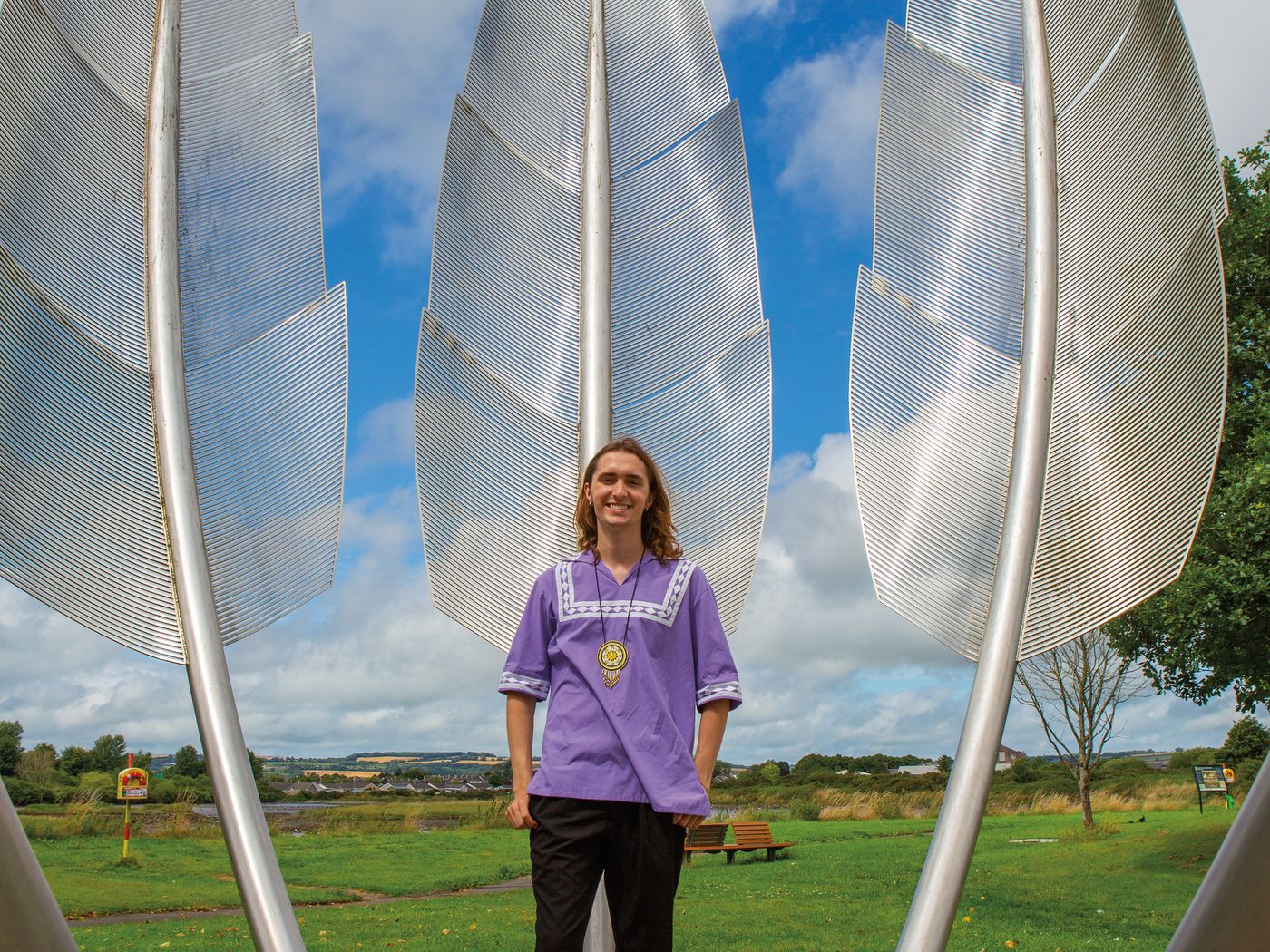 a man in purple shirt stands in front of a steel monument