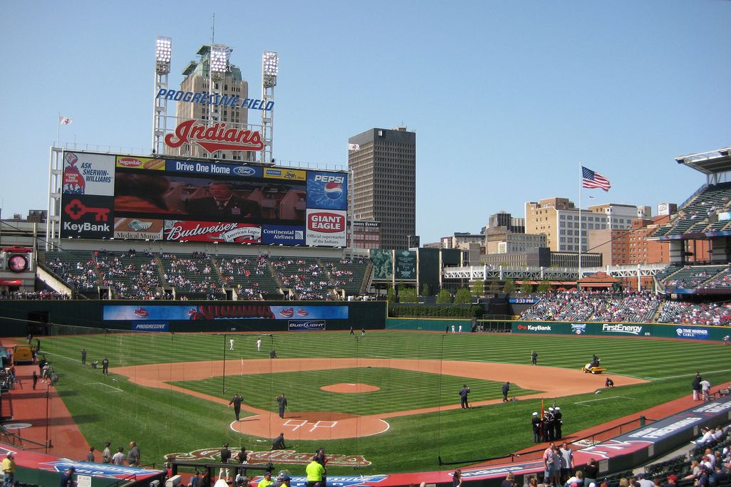 A view of a baseball field, with Indians written in red lettering above the scoreboard and crowds filling the stands