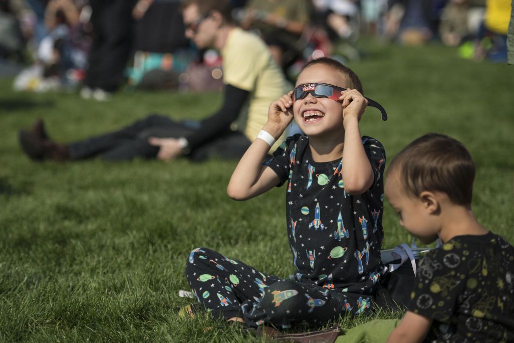 Little boy wearing eclipse glasses and smiling up toward the sky