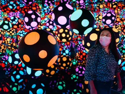 A museum patron enjoys Yayoi Kusama&#39;s latest work,&nbsp;Infinity Mirrored Room&mdash;My Heart Is Dancing into the Universe&nbsp;(2018), where paper lanterns and dots endlessly multiply inside the chamber.