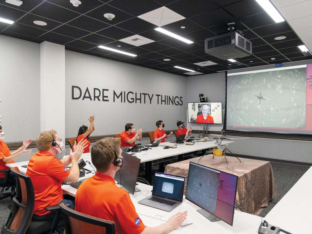 team of people in orange shirts sitting and clapping while looking at a screen