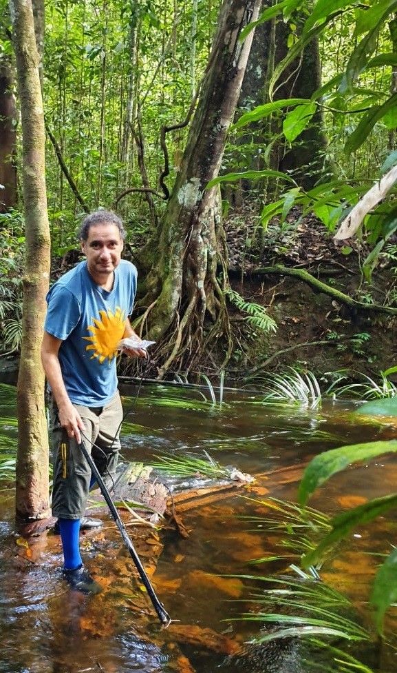 A man stands with a stick in shallow water.