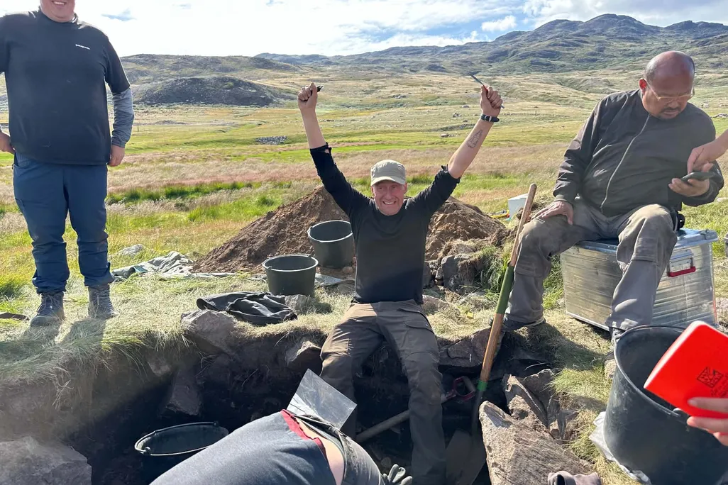 A man with his arms raised above his head in triumph, near several other people at an archaeological site