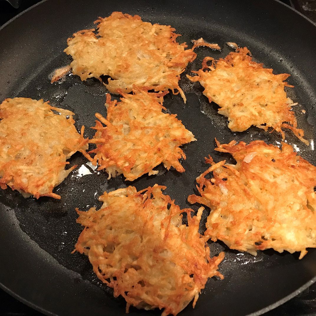 Golden brown potato pancakes frying in a pan.