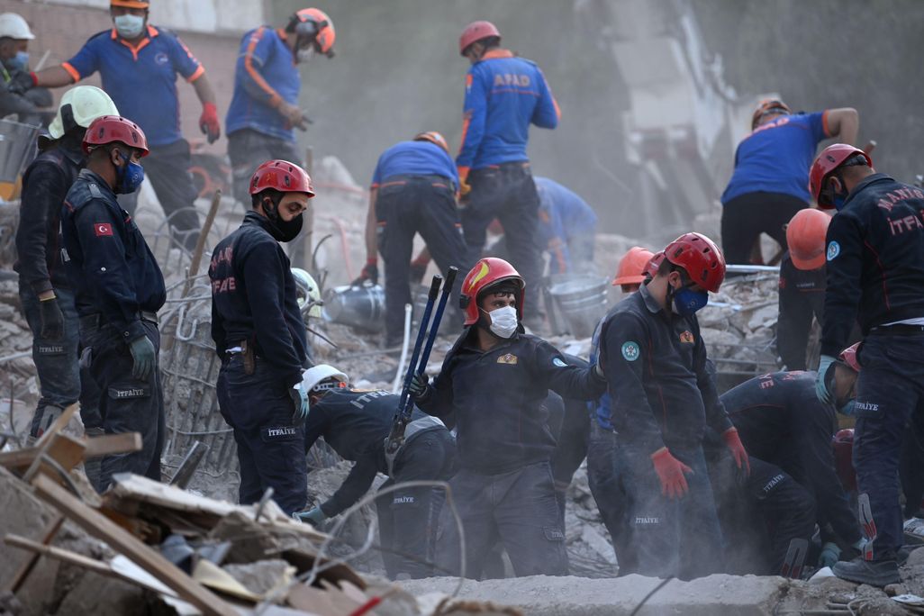 Search and rescue workers in red helmets look through debris for survivors of the October 30 earthquake