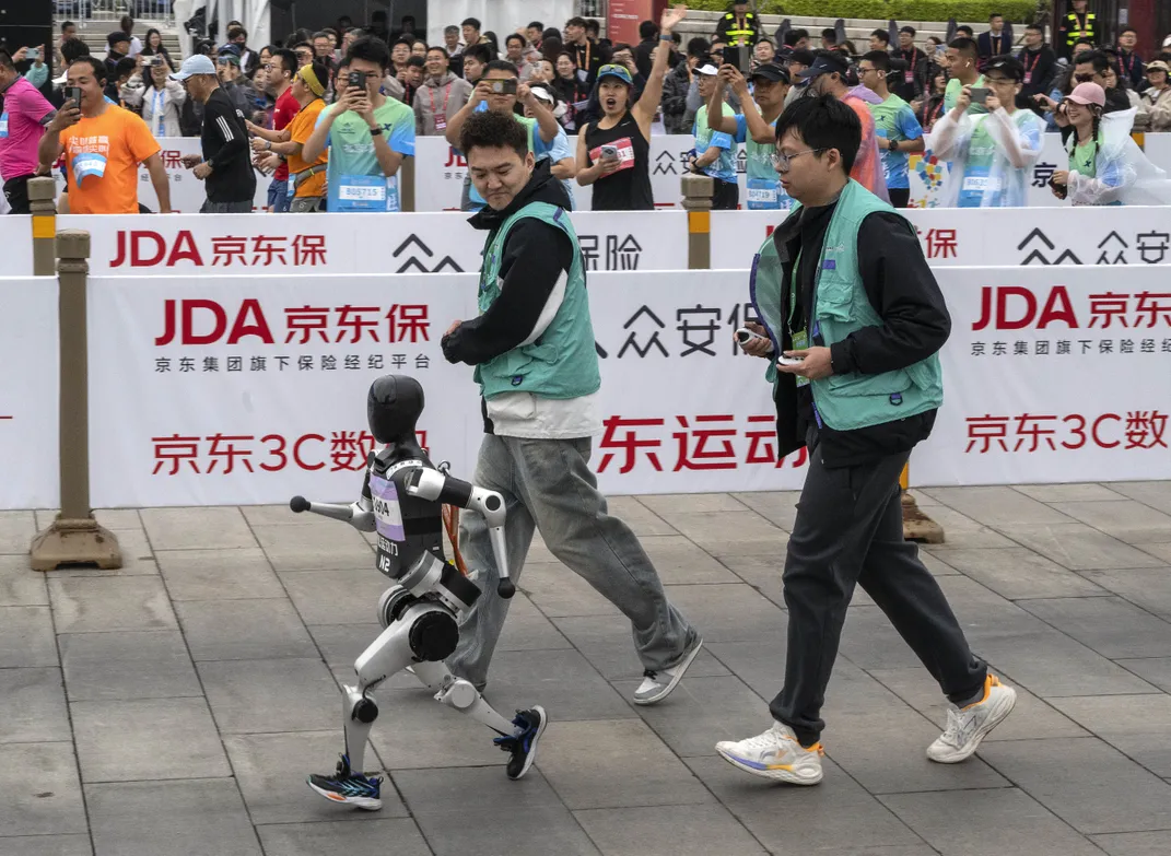 A small humanoid contestant is closely followed by its technicians