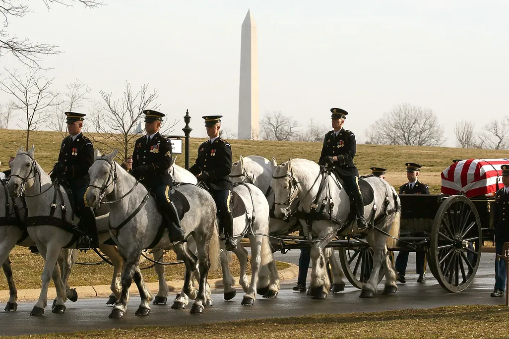 Horses with military people riding them and pulling a casket