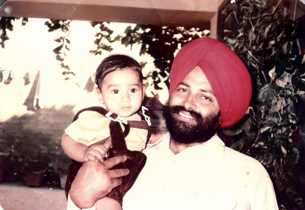 A snapshot of a man in a turban holding a toddler in overalls.