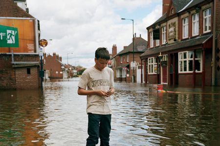 A teenage boy sends a text message on his mobile phone as stands in the floodwater on the main street of Bentley in Doncaster.