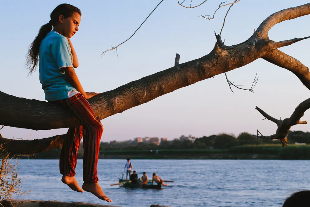 A girl sitting on the tree trunk facing the Nile.