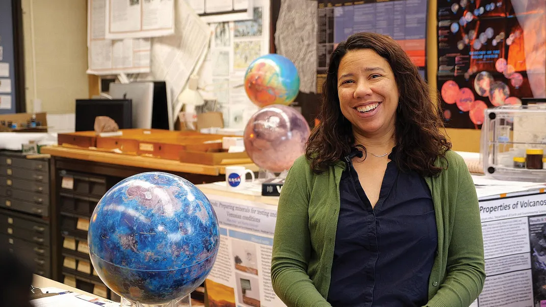 Martha Gilmore smiles in office with two globes