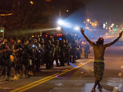 A protestor holding his hands up chants "Hands up, don't shoot" as SWAT police unit stands guard during protests against police killing of Michael Brown in Ferguson, Missouri, the United States, around midnight of Aug. 18, 2014.