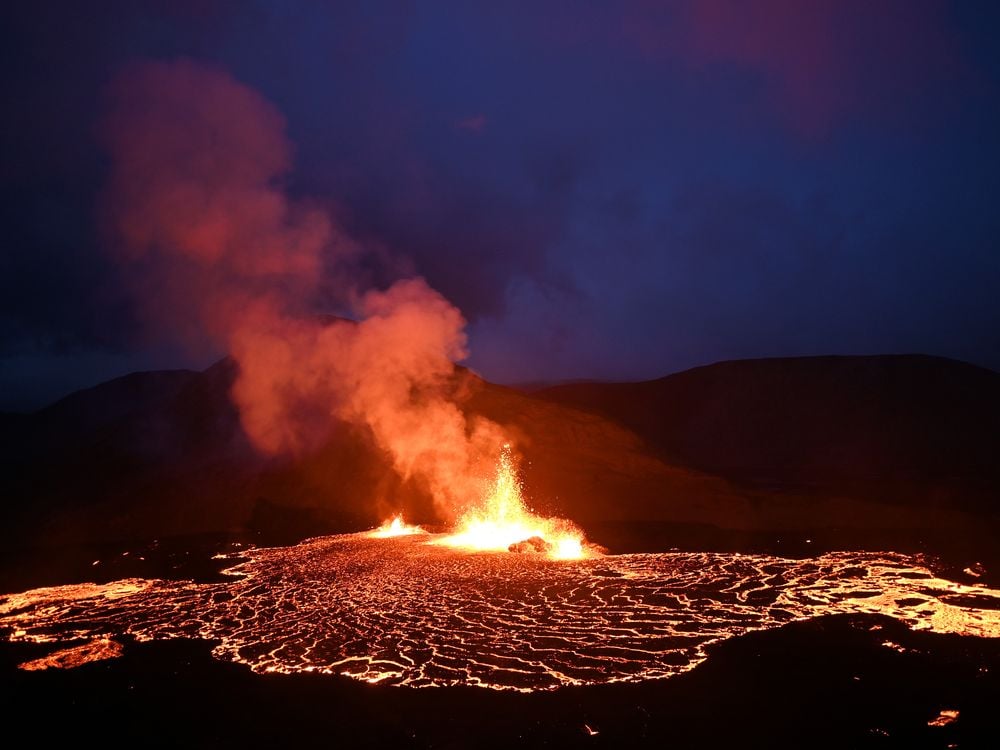 Lava and smoke rise from the volcano in the dark, surrounded by a ring of glowing lava
