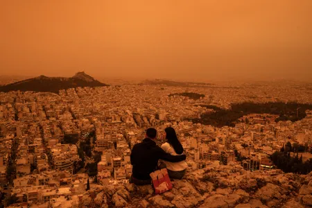A couple sits atop Tourkovounia Hill in Athens as clouds of Saharan dust cover the capital city.