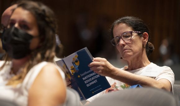Woman with brown hair and glasses reads through a print program with the words "Smithsonian National Education Summit"