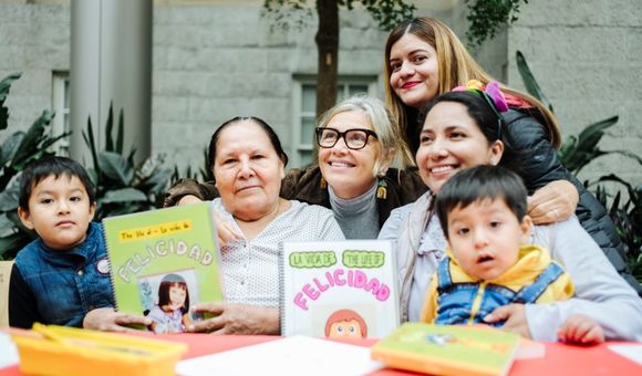 Woman smiles at the center of a group with young children and their mothers showcasing books they created