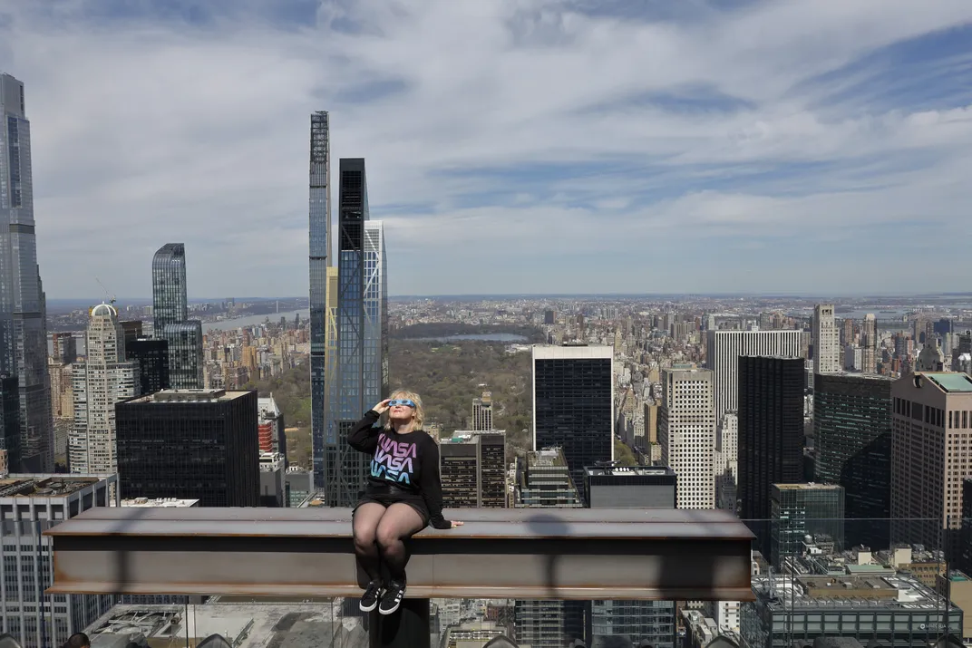 Woman sitting on beam on New York skyline watching eclipse