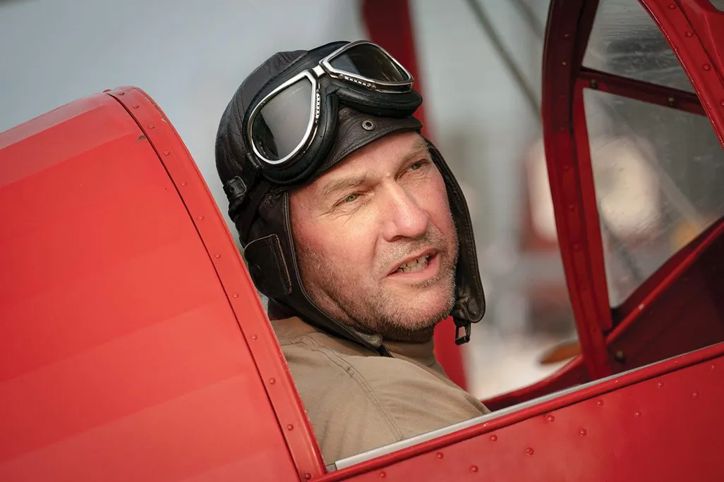 Andrew King wearing a vintage helmet and goggles in red cockpit