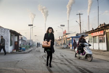 A young woman walks through gritty neighborhood streets beneath smokestacks at Datong No. 2 Power Station at dawn.