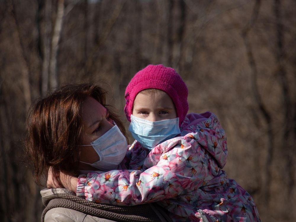 A photo of a woman holding a small child in her arms. Both are wearing masks.