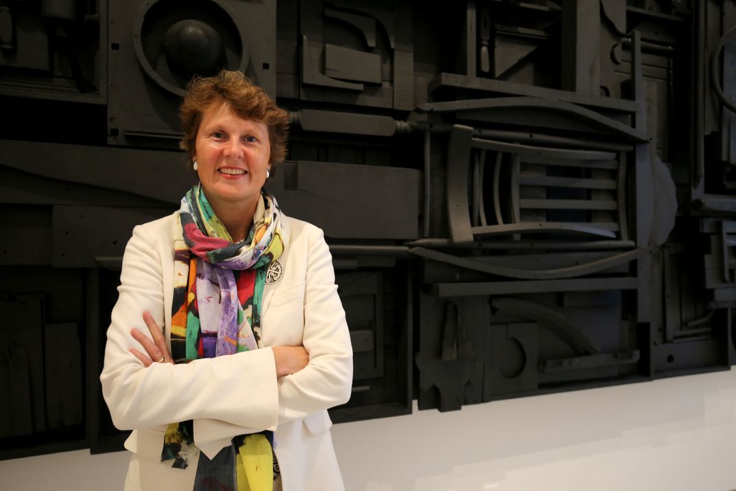 A woman standing with arms crossed in front of a large black artwork.