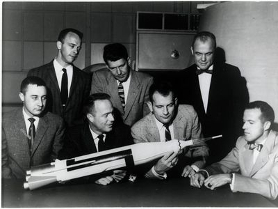 John Glenn, standing top right, looks at a model of the ship that took him to space with other astronauts from the Mercury space program in an undated photograph.
