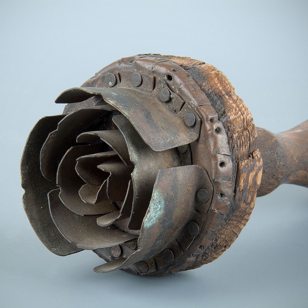 A tool with a wooden handle and concentric metal petals on one end resembling a flower.