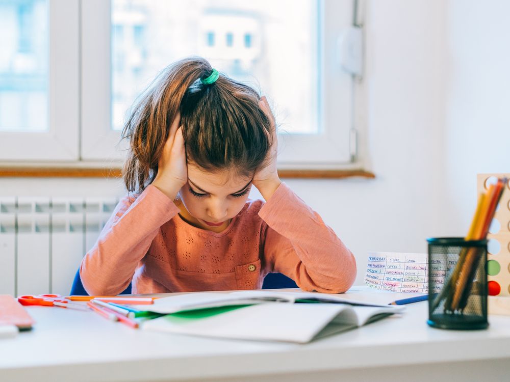 A young girl has her hands on the side of her head as she reads at a desk