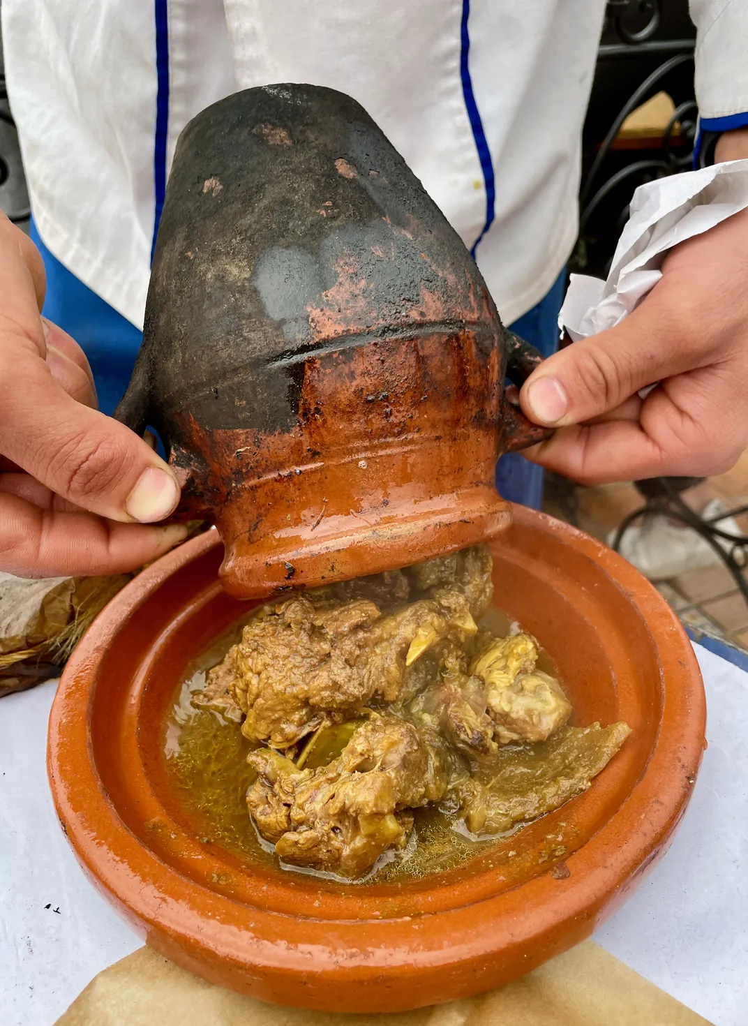 A man pours tanjia onto a ceramic plate