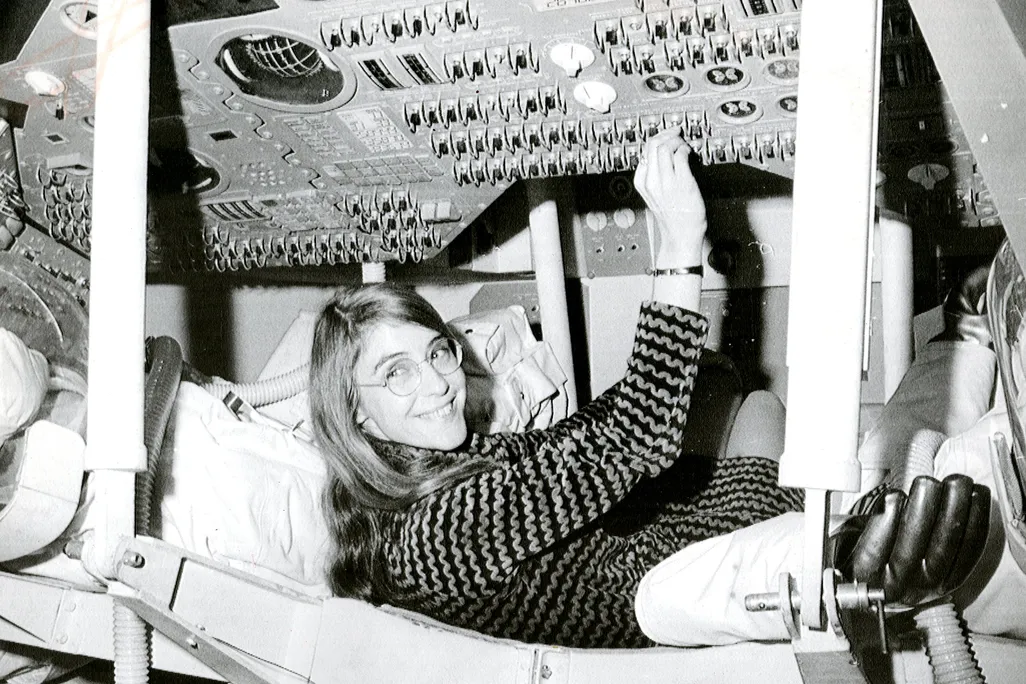 a black and while image of Hamilton reaching for a panel covered in switches