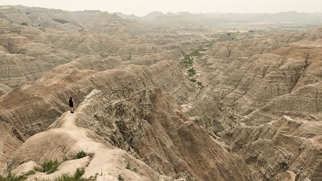 A solitary hiker nears the peak of the barren Pinnacles Overlook in Badlands National Park