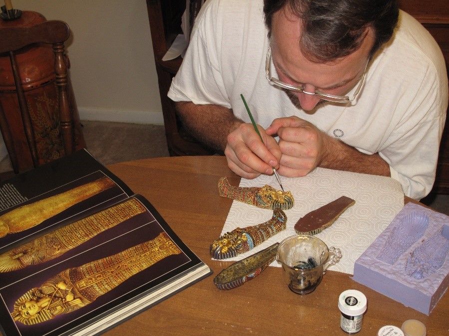 Eric Hollinger sitting at a small, wooden table painting edible gold on a small chocolate sarcophagus. 