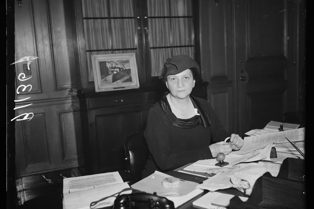 Woman wearing a hat and sitting at a desk with lots of papers on it