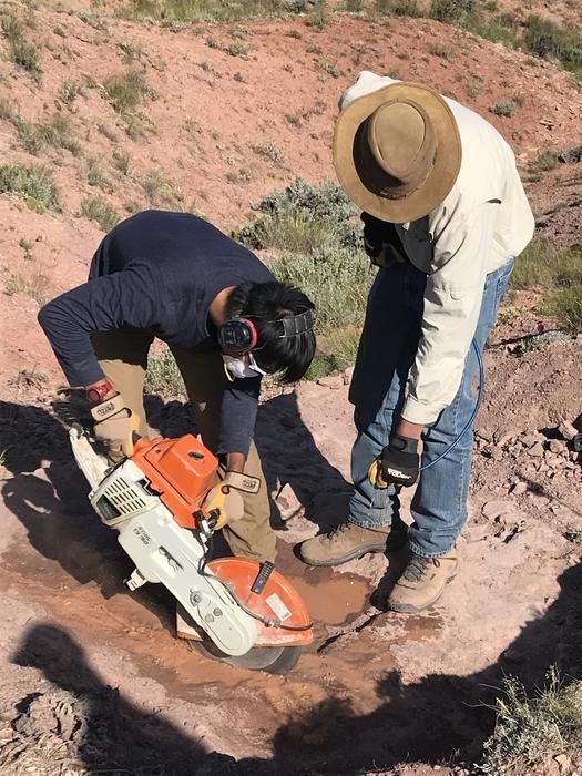 two people operating an orange and white saw in red rock