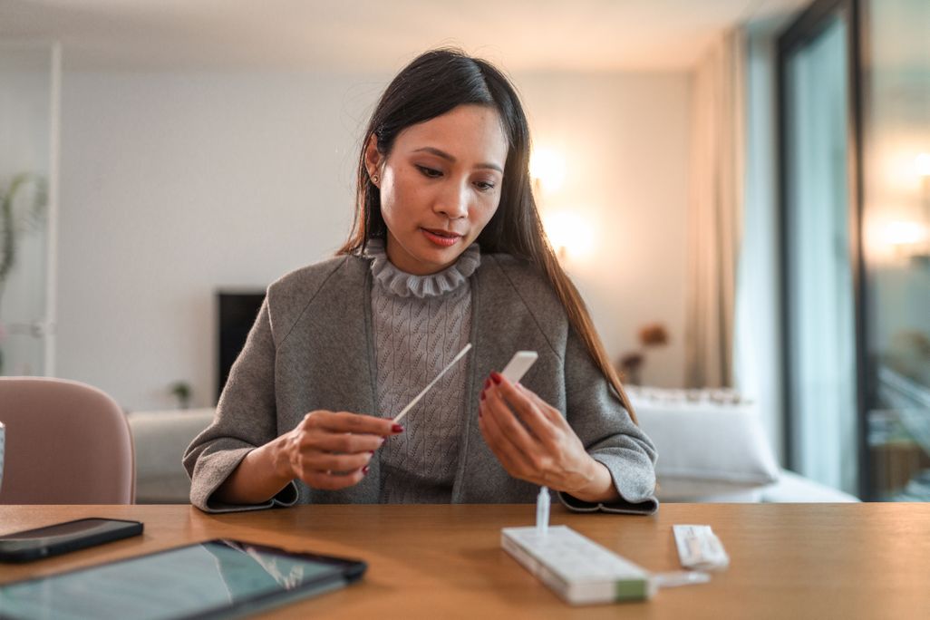 An asian woman takes an at home covid test and waits for the results at her table