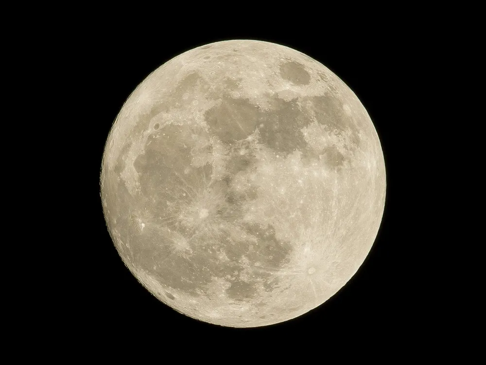 An image of the moon in front of a black sky. The moon is illuminated, and its craters is visible in various shades of white and gray.