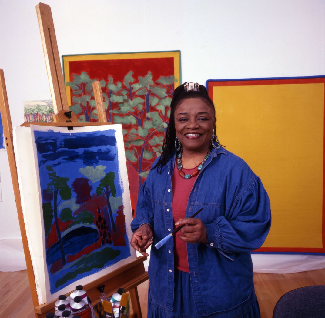 black woman holding paint brush in front of canvas with flowers painted on
