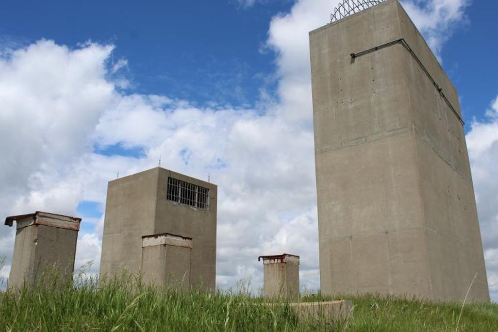 A view of four large rectangular buildings made of smooth concrete, framed against a blue sky with white, fluffy clouds