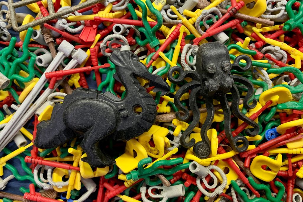 An image of random pieces of Legos that were recovered from beaches in England. In the image there is two large black lego pieces. One is an octopus and the other is a dragon.