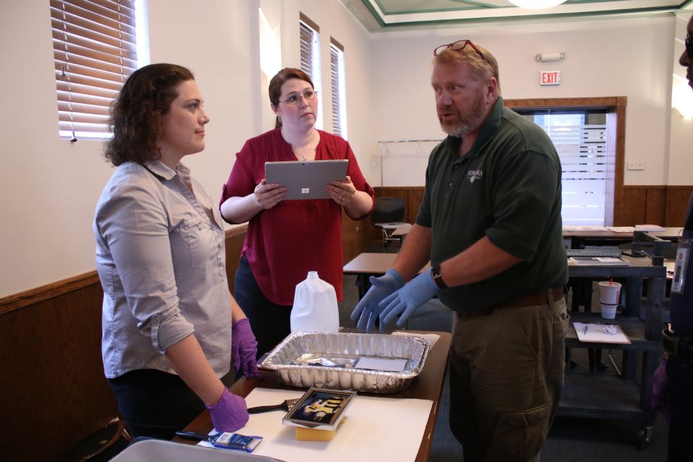 Two caucasian women and a caucasian man talk around a rectangular table. 